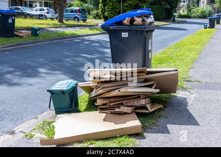 Mülltonnen und überlaufende Kartonverpackungen warten auf Müllabfuhr in einer Vorstadtstraße in Woking, Surrey, SE England Stockfoto