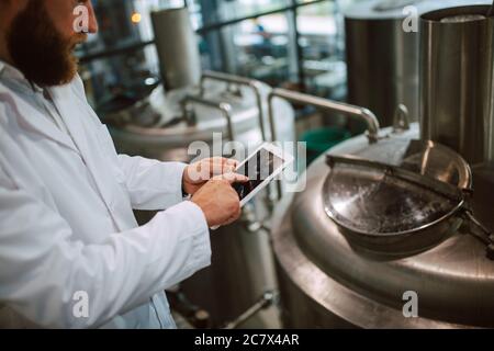 Nahaufnahme von Tablet-Computer in der Hand von professionellen kaukasischen Technologen Experten in weißen Uniform in Produktionsanlage - Lebensmittel-oder Getränkefabrik Stockfoto