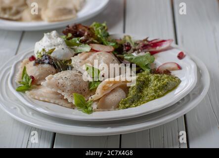 Italienische Ravioli serviert mit Pesto, Salat und Sahne auf weißem Teller, Holzboden, Kopierraum Stockfoto