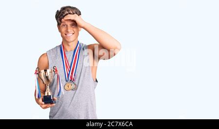 Junger, hübscher Mann mit Siegertrophäe, der mit gestressten und frustrierten Medaillen mit der Hand am Kopf, überrascht und wütend ins Gesicht tragt Stockfoto