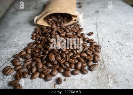 Geröstete Arabica Kaffeebohnen verteilen sich auf einem Tisch mit einem hessischen Sack im Hintergrund. Die Bohnen werden nativ auf den Philippinen angebaut. Stockfoto