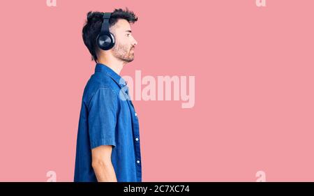 Junger hispanischer Mann, der Musik hört, mit Kopfhörern, die zur Seite schauen, entspannen Sie sich in der Profilpose mit natürlichem Gesicht und selbstbewusem Lächeln. Stockfoto