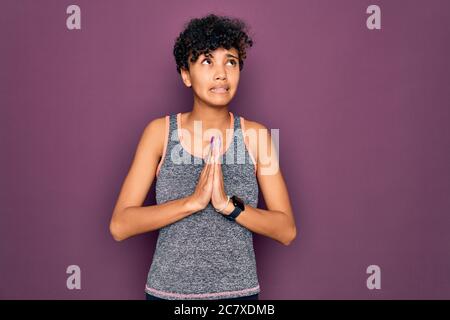 Junge schöne afro amerikanische Sportlerin tun Übung tragen Sportkleidung Betteln und beten mit Händen zusammen mit Hoffnung Ausdruck auf fa Stockfoto