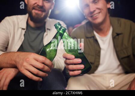 Nahaufnahme von zwei männlichen Freunden lächeln und klirren Bierflaschen, während Film im Kino, Kopierraum Stockfoto