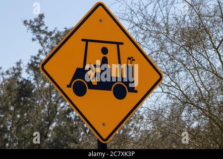 Diamantförmiges gelbes Schild mit schwarzer Grafik, die einen Golfwagen gegen einen blauen Himmel und Bäume zeigt Stockfoto