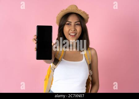 Junge Frau hält Handy in der Nähe im Vordergrund vor schlichtem rosa Hintergrund Stockfoto