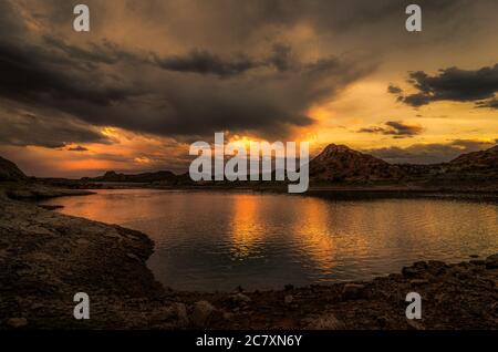 See umgeben von Hügeln, die unter dem wunderschönen Sonnenuntergang glänzen Stockfoto