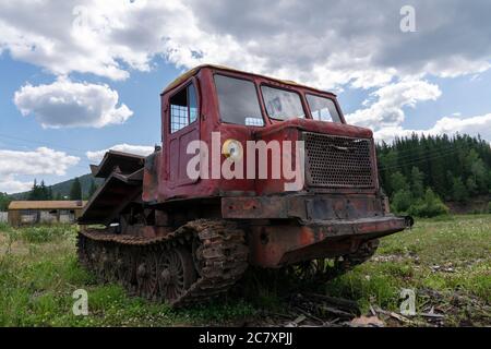 Ein alter Holzfäller, rostig und auf einem Feld vor dem Hintergrund eines schönen Waldes verlassen, als Symbol für den Zusammenbruch der Industrie in Russland und Stockfoto