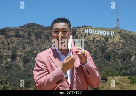 Hollywood, Kalifornien, USA. Juli 2020. TV-Moderator Joey Zhou zieht seine Maske vor dem Hollywood-Schild während seiner COVID-19 Pandemie-Interview-Show in Hollywood, Kalifornien. Joey Zhou ist Gastgeber der "Zhou Zheng Show" und Gründer von Beverly Arts und der Beverly News. Sheri Determan/Alamy.com Stockfoto