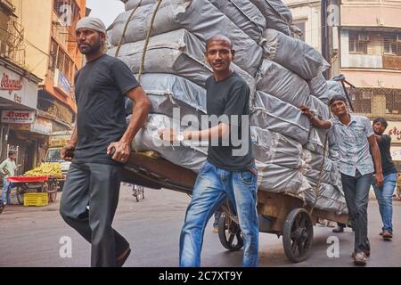 Ein Handwagen voller Stoffballen, der von vier Männern entlang der Kalbadevi Road, einem Textilhandelsgebiet im Bhuleshwar-Gebiet Mumbai, Indien, transportiert wurde Stockfoto