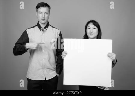 Porträt von jungen gut aussehenden Geschäftsmann und reifen asiatischen Geschäftsfrau zusammen mit weißen Brett Stockfoto