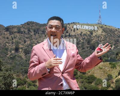 Hollywood, Kalifornien, USA. Juli 2020. TV-Moderator Joey Zhou spricht mit der Kamera, während er seine Maske während seiner COVID-19 Pandemie-Interview-Show auf dem Hollywood-Schild in Hollywood, Kalifornien, hält. Joey Zhou ist Gastgeber der "Zhou Zheng Show" und Gründer von Beverly Arts und der Beverly News. Sheri Determan/Alamy.com Stockfoto