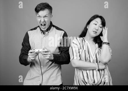 Junge gut aussehende Geschäftsmann und reifen asiatischen Geschäftsfrau vor grauem Hintergrund Stockfoto
