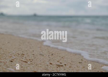 Extreme Nahaufnahme Sand und Steine Details am Strand. Verschwimmen Sie den grünen Meereshorizont und den Wellenhintergrund. In Boracay Island Philippinen Stockfoto