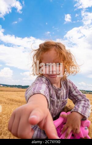 Schönes kleines Mädchen steckt ihren Finger in die Kamera vor dem Hintergrund des blauen Himmels und weißen Wolken. Stockfoto