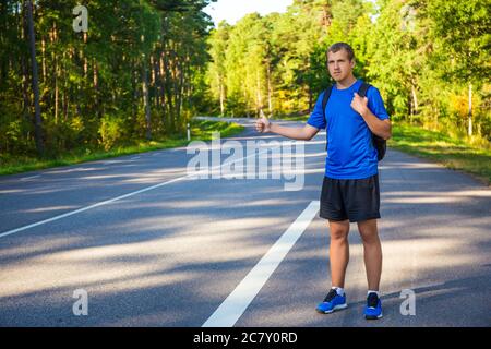 Junger, hübscher Mann, der auf der Waldstraße trampte Stockfoto