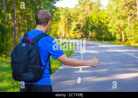 Rückansicht des jungen Mannes, der auf der Waldstraße trampte Stockfoto