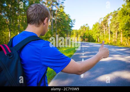 Anhalter-Konzept - Rückansicht des Mannes mit Rucksack auf Waldstraße stehen Stockfoto