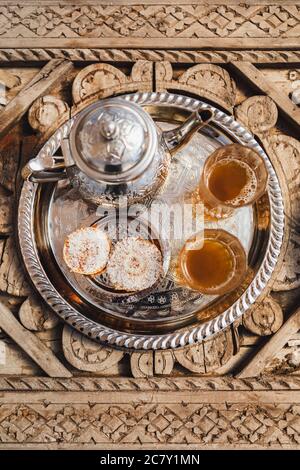 Traditioneller marokkanischer Minztee mit Plätzchen auf silbernem Tablett auf geschnitztem Holztisch. Schöner Vintage-Stil, Gastfreundschaft in Marokko. Stockfoto