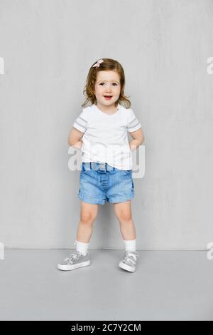 Zwei Jahre altes Mädchen in weißen T-Shorts und Jeans Shorts posiert im Studio Stockfoto