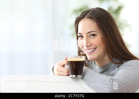 Glückliche Frau mit Kaffeetasse Blick auf Kamera sitzen auf dem Sofa zu Hause Stockfoto