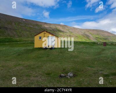 Blick auf Latrar Campingplatz in adalvik Bucht mit gelben Notunterstand Hütte in West Fjorden Hornstrandir in Island, mit grünen Wiese, Hügel Stockfoto