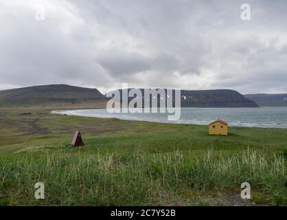 Blick auf Latrar Campingplatz in adalvik Bucht mit gelben Notunterstand Hütte in West Fjorde Naturschutzgebiet Hornstrandir in Island, mit grünem Gras Stockfoto