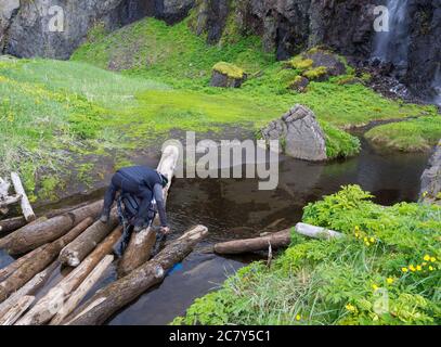 Mann Wanderer, der auf Holzbalken steht, nimmt sauberes Wasser auf und füllt sich Stockfoto