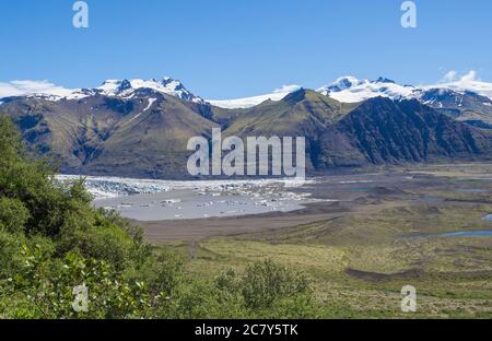 Blick auf die Gletscherlagune mit Eisbergen und Zunge des Skaftafellsjokull, Vatnajokull Sporn und bunte schneebedeckte Rhyolit Berge in Skaftafell Stockfoto