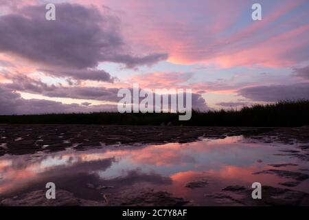 Bunte Sonnenuntergang Wolken Himmel und Reflexion in Pfützen Wasser. Niedriger Winkel Stockfoto