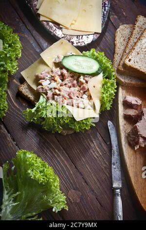 Thunfisch-Sandwich mit grünem Salat, Käse, frischen Gurken und Weizenbrot, auf Holz dunkel rustikalen Tischhintergrund, niemand Stockfoto