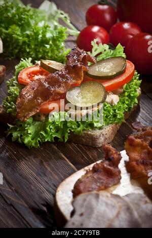 Sandwich mit geräuchertem Fleisch, grünem Salat, frischen Tomaten, eingelegten Gurken und Roggenbrot, auf Küche rustikalen Holztisch Hintergrund, niemand Stockfoto