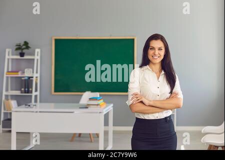 Lehrerin mit gekreuzten Armen in leerem Klassenzimmer. Professor in der Schule, bereit, den Unterricht zu beginnen Stockfoto