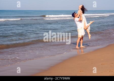 Glückliches Paar am goldenen Sandstrand. Mann, der die Frau in den Armen hält mit Liebe Stockfoto
