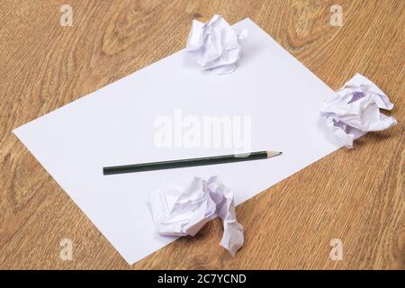 Schwarzer Bleistift auf klarem weißen Papier mit zerbröckeligen Papierkugeln auf Holztischhintergrund Stockfoto