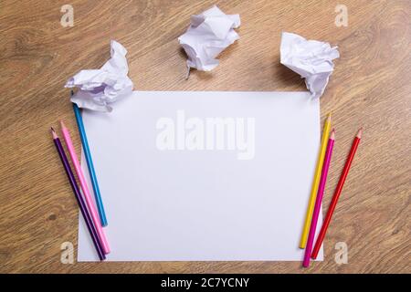 Bunte Bleistifte auf klarem weißem Papier mit zerbröckeligen Papierkugeln auf Holztischhintergrund Stockfoto