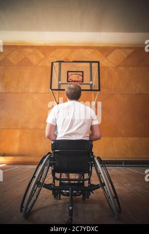 Rückansicht eines Basketballspielers in freier Wurfhaltung im Rollstuhl im Innenbereich Stockfoto