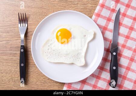Spiegelei in weißer Platte mit Gabel und Messer auf Holztisch Stockfoto