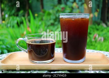 Heißer Kaffee und Eiskaffee auf Holztablett serviert auf Gartentisch Stockfoto