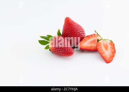 Nahaufnahme von zwei frischen ganzen Erdbeeren neben einer halbiert geschnittenen Erdbeere auf hellem Hintergrund. Gesundes und veganes Lebensmittelkonzept. Stockfoto