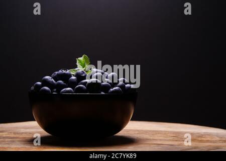 Frische Blaubeeren mit Tau und Minzblättern auf Holztisch und schwarzem Hintergrund aus nächster Nähe. Sommer Hintergrund, Rohkost für Veganer. Frisch und lecker für Stockfoto