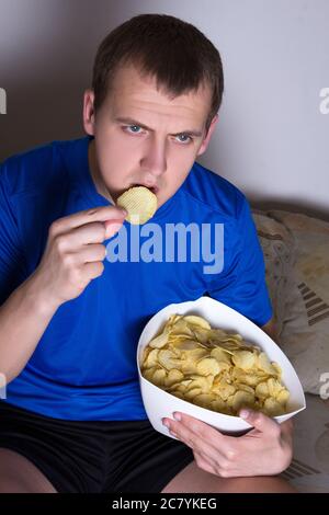 Junger attraktiver Mann, der zu Hause Fernsehen und Chips essen kann Stockfoto