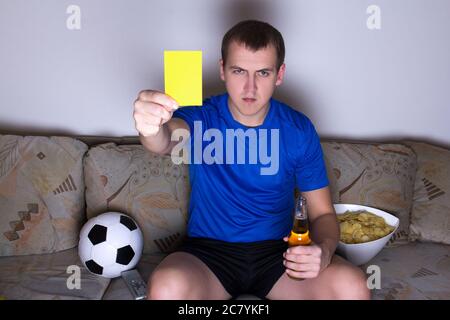 Junger Mann in Uniform beim Fernsehen und beim Ansehen von Fußball und mit gelber Karte Stockfoto