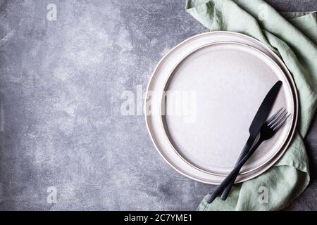 Teller, schwarzes Besteck und Leinenserviette auf Steintisch. Einstellungstabelle, Draufsicht. Stockfoto