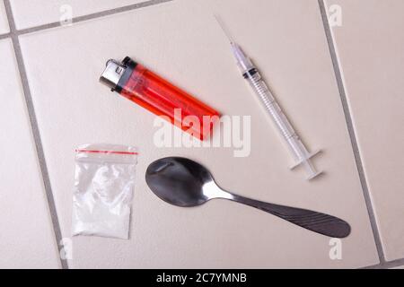 Drogenspritze, Heroinpulver in der Packung, Löffel und Feuerzeug auf Fliesenboden Stockfoto