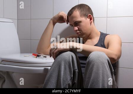 Junger depressiver Mann mit Heroinsucht im Badezimmer sitzen Stockfoto