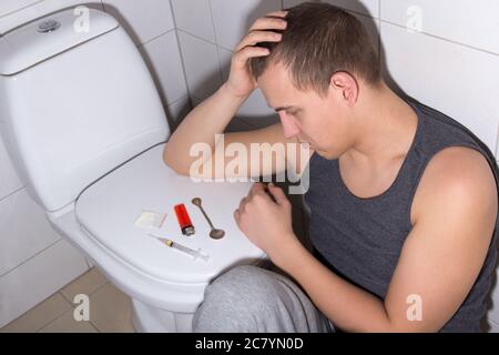 Junger Mann mit Steinen und Heroinsucht im Badezimmer Stockfoto