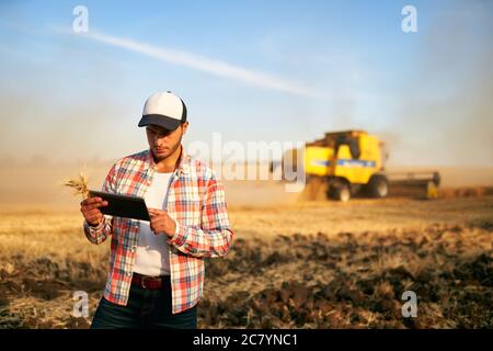 Präzisionslandwirtschaft. Landwirt hält Tablet für Mähdrescher Führung und Steuerung mit modernen Automatisierungssystem. Agronom mit Online-Daten Stockfoto