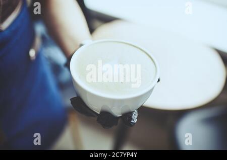 Barista trägt medizinische Latexhandschuhe, macht Cappuccino, Barkeeper bereitet Kaffee trinken. Verschwommenes Bild, selektiver Fokus Stockfoto