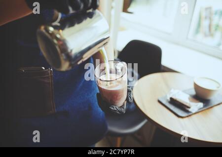 Barista macht rosa Matcha Latte mit Milch. Barkeeper bereitet leckere Getränk.verschwommenes Bild, selektiver Fokus Stockfoto